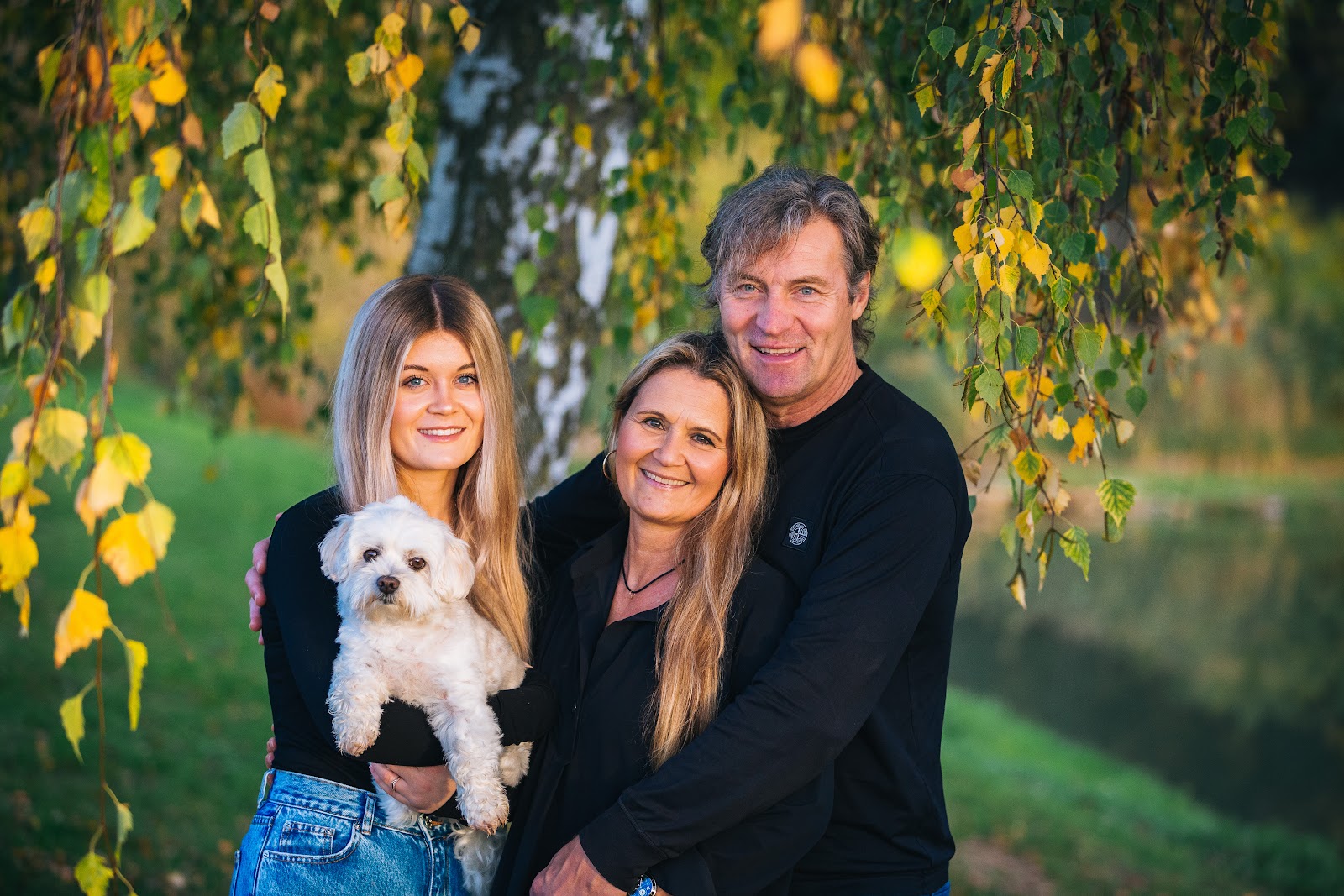 Familienfoto von Eltern mit erwachsener Tochter, die einen kleinen weißen Hund auf dem Arm hält, fotografiert von Simone Emmert